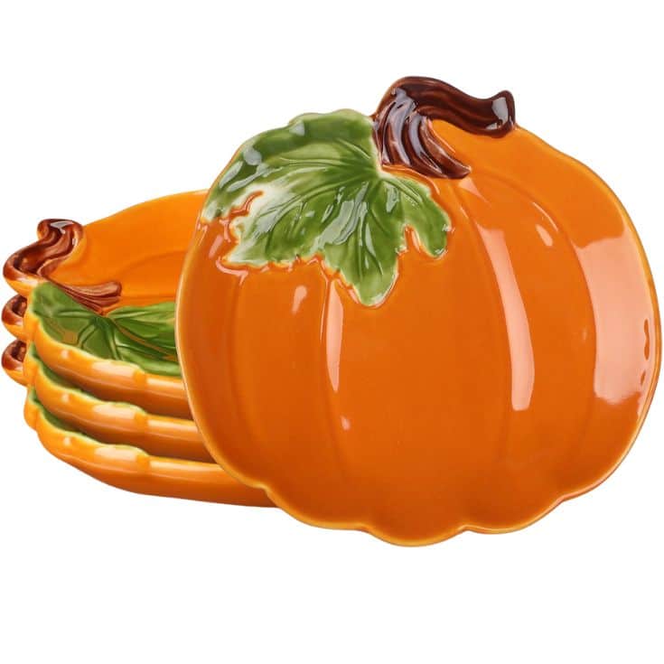 Four ceramic plates shaped and painted like pumpkins, stacked together. The plates are orange with green leaves and brown stems, designed for a festive or autumn-themed table setting.