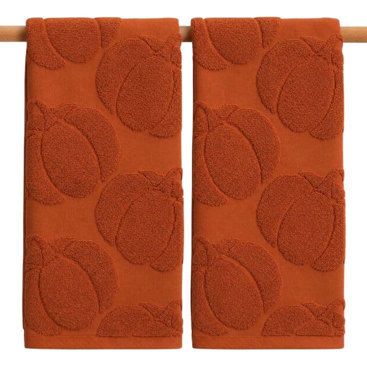 Two orange towels hang on a wooden rod, each featuring a raised pumpkin pattern for a textured, autumn-inspired design.