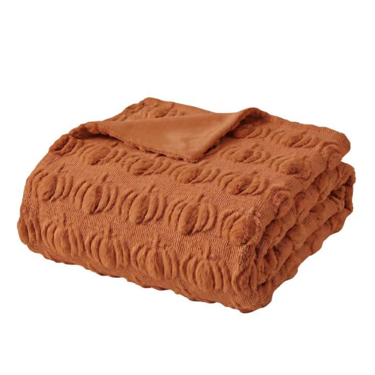 A folded, textured burnt orange blanket with a raised circular pattern, shown on a plain white background.
