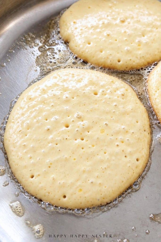 Pancakes cooking in a skillet with bubbles forming on the surface before flipping