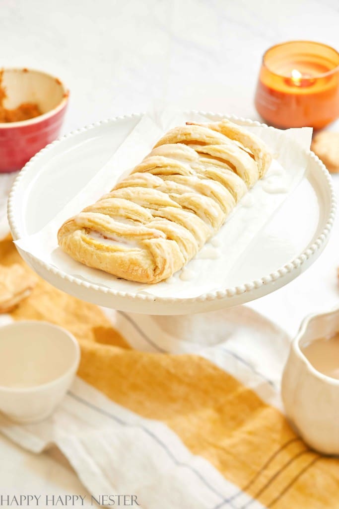 Braided pumpkin puff pastry dessert served on a white platter with a light glaze.