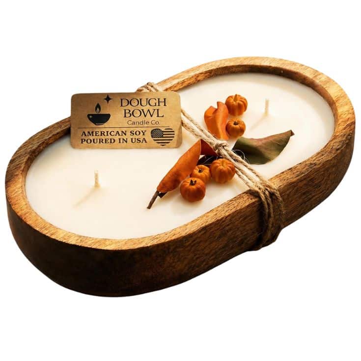 A wooden dough bowl candle with two wicks, decorated with dried orange berries and leaves, tied with twine. A label reads “Dough Bowl Candle Co. American Soy Poured in USA.”.