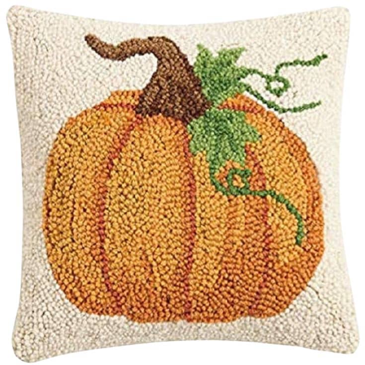 Square pillow with a textured design of an orange pumpkin, green leaves, and brown stem on a white background. The pillow has a hooked, tufted fabric style.