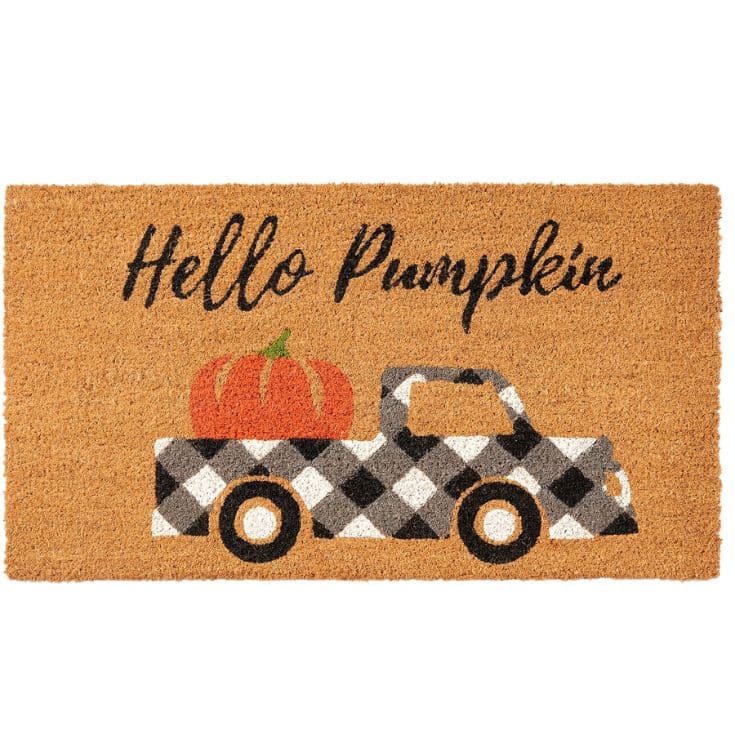 A doormat with “Hello Pumpkin” written above a black-and-white checkered truck carrying a large orange pumpkin in its bed.