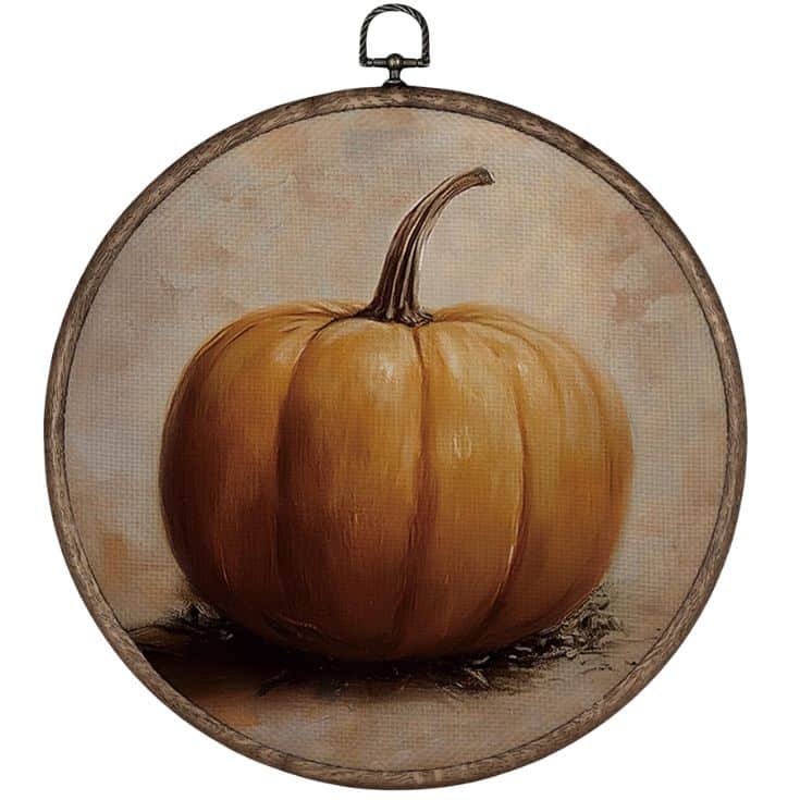 A realistic painting of an orange pumpkin with a stem, displayed inside a round wooden embroidery hoop against a soft, neutral background.