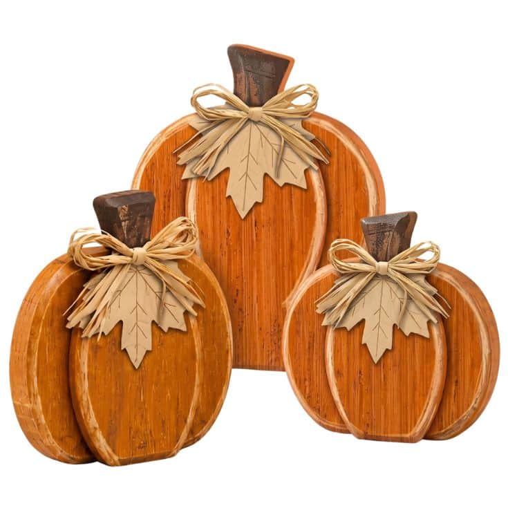 Three decorative wooden pumpkins, each adorned with a raffia bow and a tan leaf, are grouped together. The pumpkins are different sizes and have a rustic, autumn-themed design.