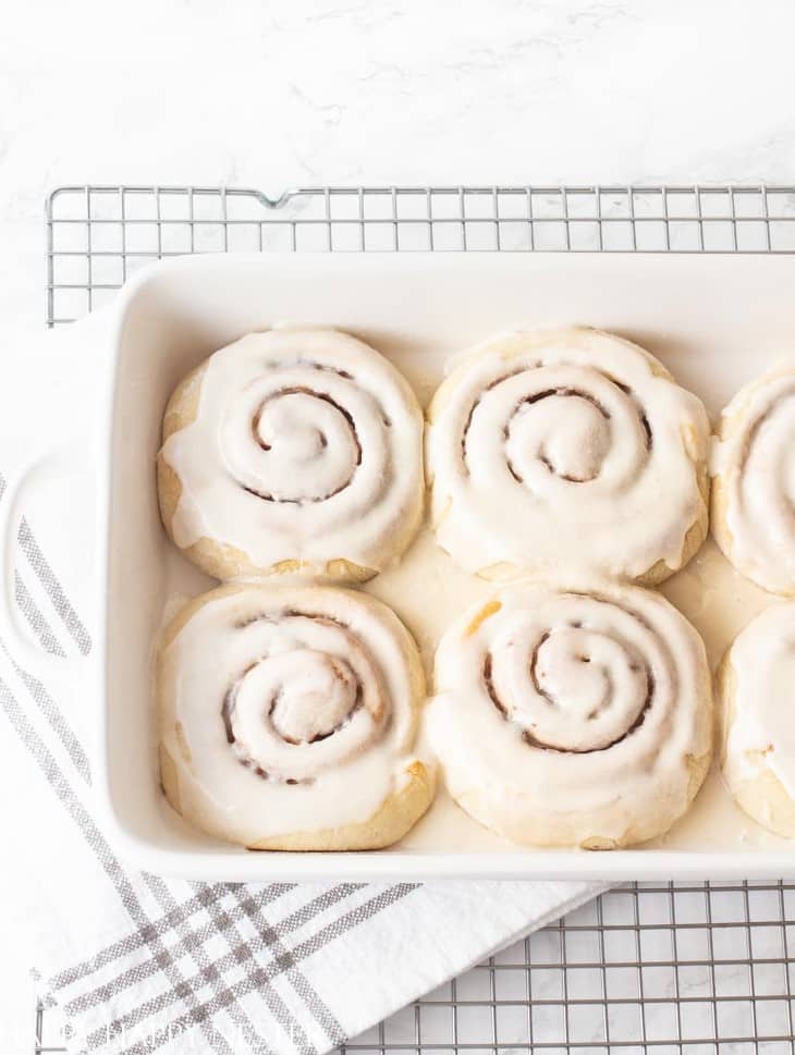 Four homemade cinnamon rolls topped with white frosting in a baking dish on a cooling rack.