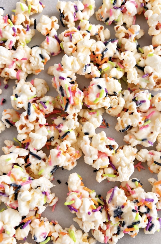 Close-up of popcorn coated in a creamy white coating and topped with pink, orange, green, purple, and black sprinkles.
