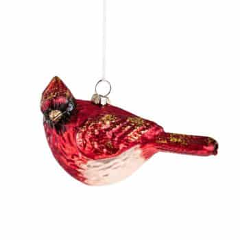 Red cardinal glass ornament hanging from a pine branch.