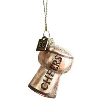 Anthropologie Cheers glass Christmas ornament hanging from an evergreen branch.