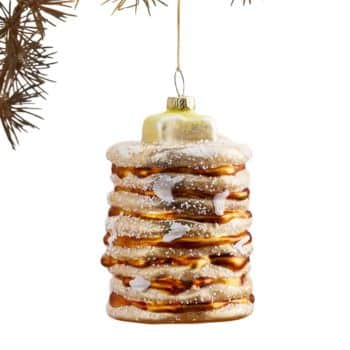 Stack of pancakes glass Christmas ornament hanging from an evergreen tree.