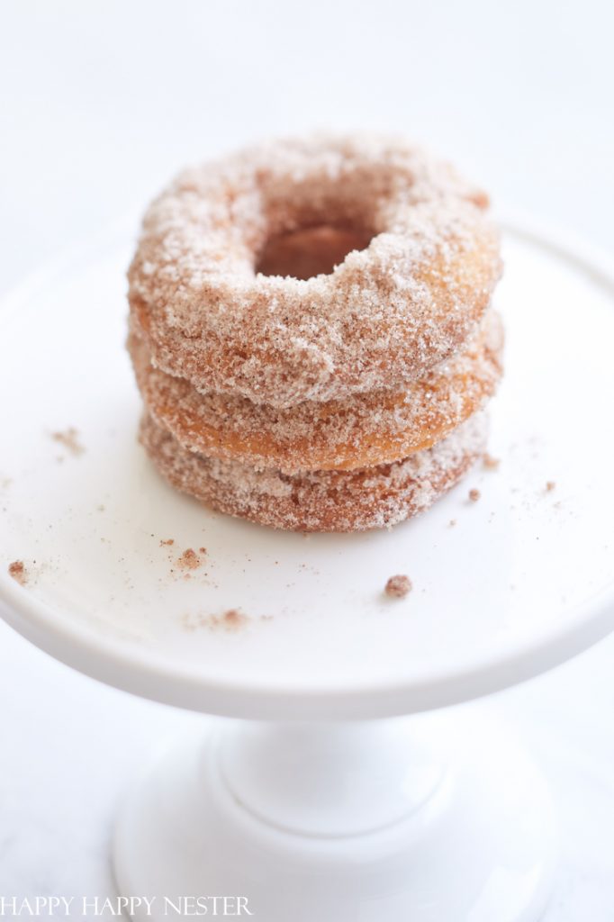 A stack of three cinnamon-sugar donuts on a white pedestal cake stand, perfect for holiday brunch ideas.