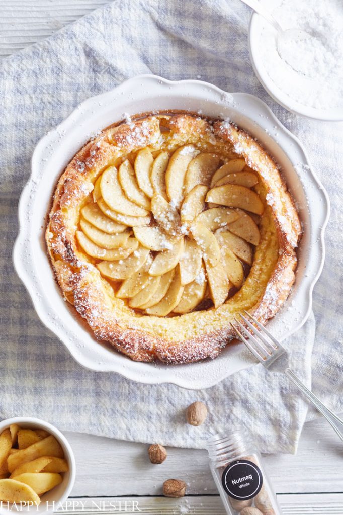An apple Dutch baby pancake topped with powdered sugar in a white scalloped baking dish, perfect for holiday brunch ideas.