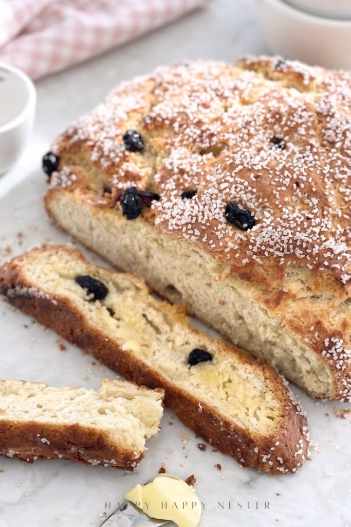 A loaf of Irish soda bread with raisins and coarse sugar crystals, with two buttered slices perfect for holiday brunch ideas.
