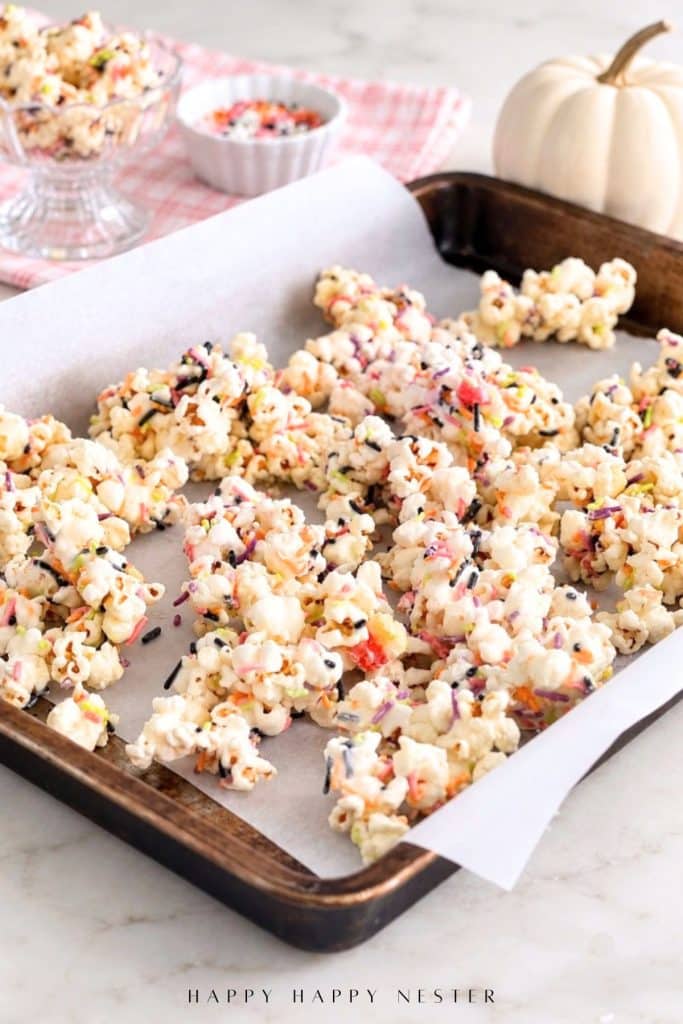 Coated popcorn with colorful sprinkles and candies on a parchment-lined baking sheet.