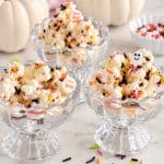 Halloween popcorn with colorful sprinkles served in glass dessert bowls with white pumpkins.