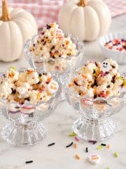 Halloween popcorn with colorful sprinkles served in glass dessert bowls with white pumpkins.