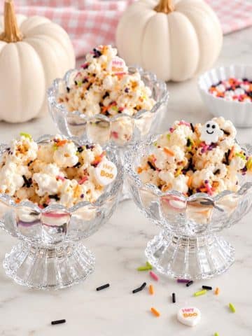 Halloween popcorn with colorful sprinkles served in glass dessert bowls with white pumpkins.