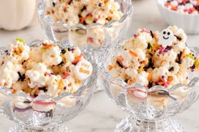 Halloween popcorn with colorful sprinkles served in glass dessert bowls with white pumpkins.