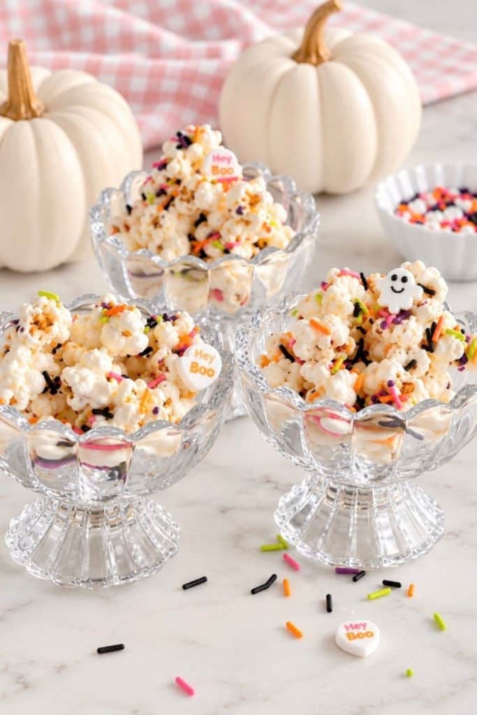 Halloween popcorn with colorful sprinkles served in glass dessert bowls with white pumpkins.