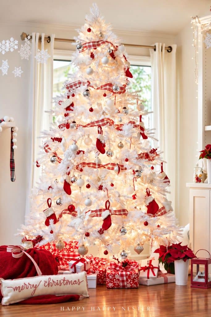 White Christmas tree decorated with red plaid ribbon, red stockings, silver and white ornaments, and warm Christmas lights.