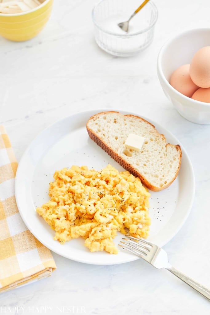 A plate of scrambled eggs seasoned with pepper next to a slice of buttered bread, perfect for holiday brunch ideas.