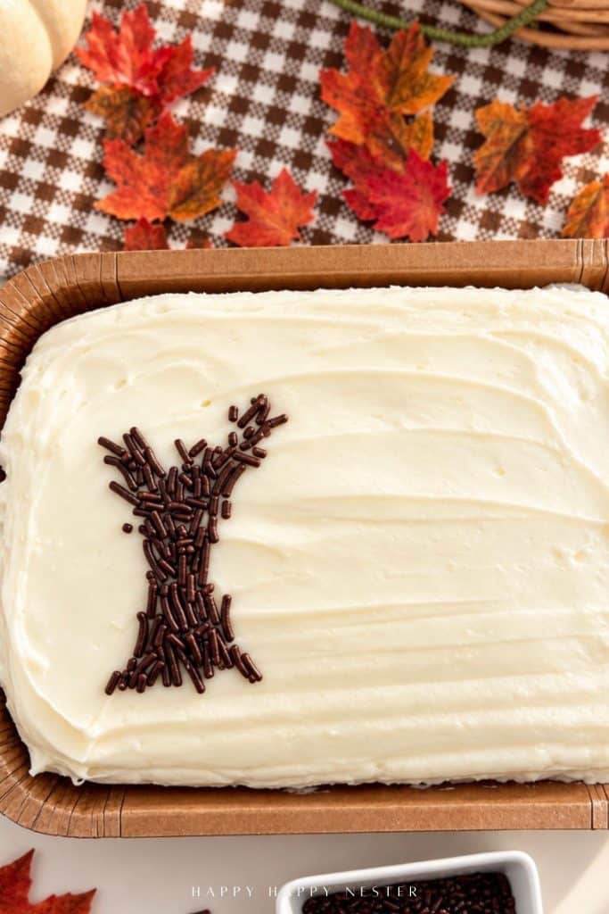 Chocolate sprinkles arranged into the trunk and branches of a tree on a white-frosted sheet cake, showing the first step of a fall cake decorating design.
