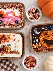 Three decorated mini sheet cakes featuring a fall sprinkle tree with pumpkins, a pink candy truck carrying pumpkins, and an orange jack-o'-lantern on chocolate frosting.