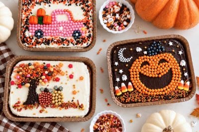 Three decorated mini sheet cakes featuring a fall sprinkle tree with pumpkins, a pink candy truck carrying pumpkins, and an orange jack-o'-lantern on chocolate frosting.
