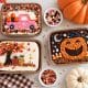 Three decorated mini sheet cakes featuring a fall sprinkle tree with pumpkins, a pink candy truck carrying pumpkins, and an orange jack-o'-lantern on chocolate frosting.