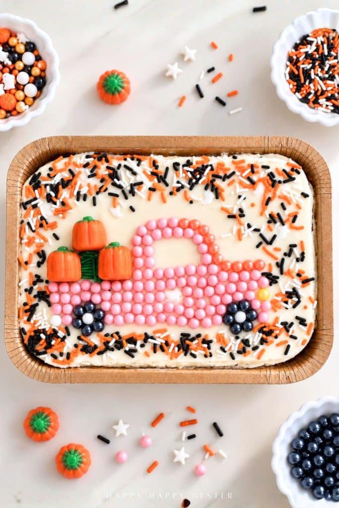 Trader Joe's mini sheet cake decorated with a pink candy pearl pickup truck carrying orange pumpkins and surrounded by Halloween sprinkles.